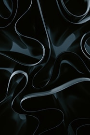 Abstract, flowing shapes with a glossy, dark appearance create a sense of depth and motion. The texture appears smooth and almost liquid-like.