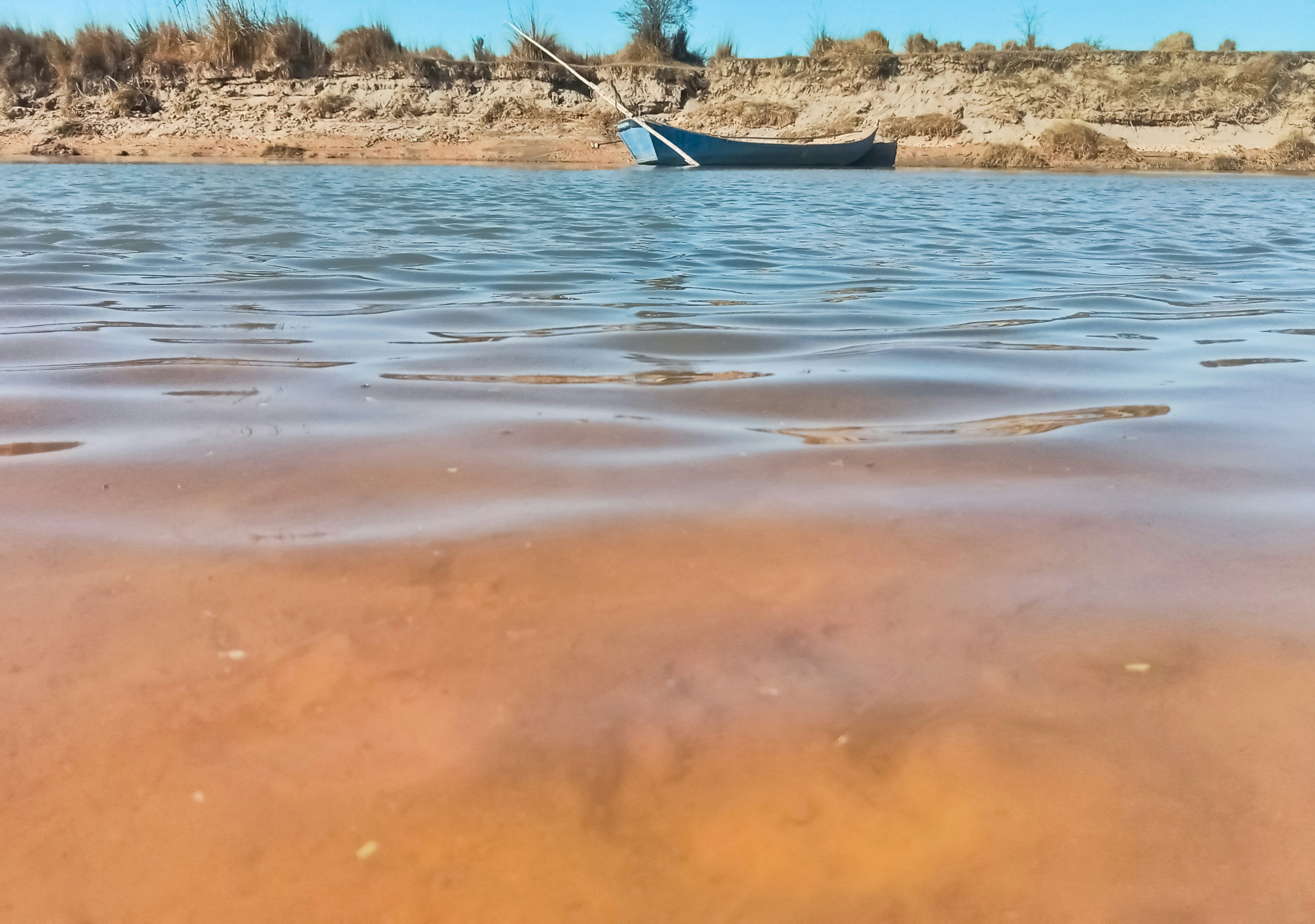 a boat floating on top of a lake next to a sandy shore