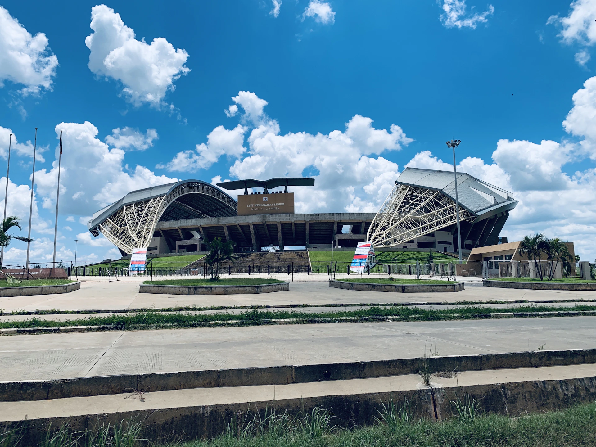 An outside view of a famous stadium showcasing its iconic architecture against a clear blue sky, with excited fans streaming through the gates.