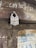 A close-up view of a metal padlock attached to a loop on a wooden door. The padlock has visible text and appears worn, indicating age. Chalk writings are on the upper part of the door, and faded posters featuring text and images are pasted below.