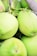 Several green coconuts are clustered closely together. The coconuts have smooth, slightly textured surfaces typical of fresh unripe coconuts. Their natural, bright green color suggests they are young and fresh. Thin stems and remnants of their fibrous husks are visible, indicating they are freshly harvested.