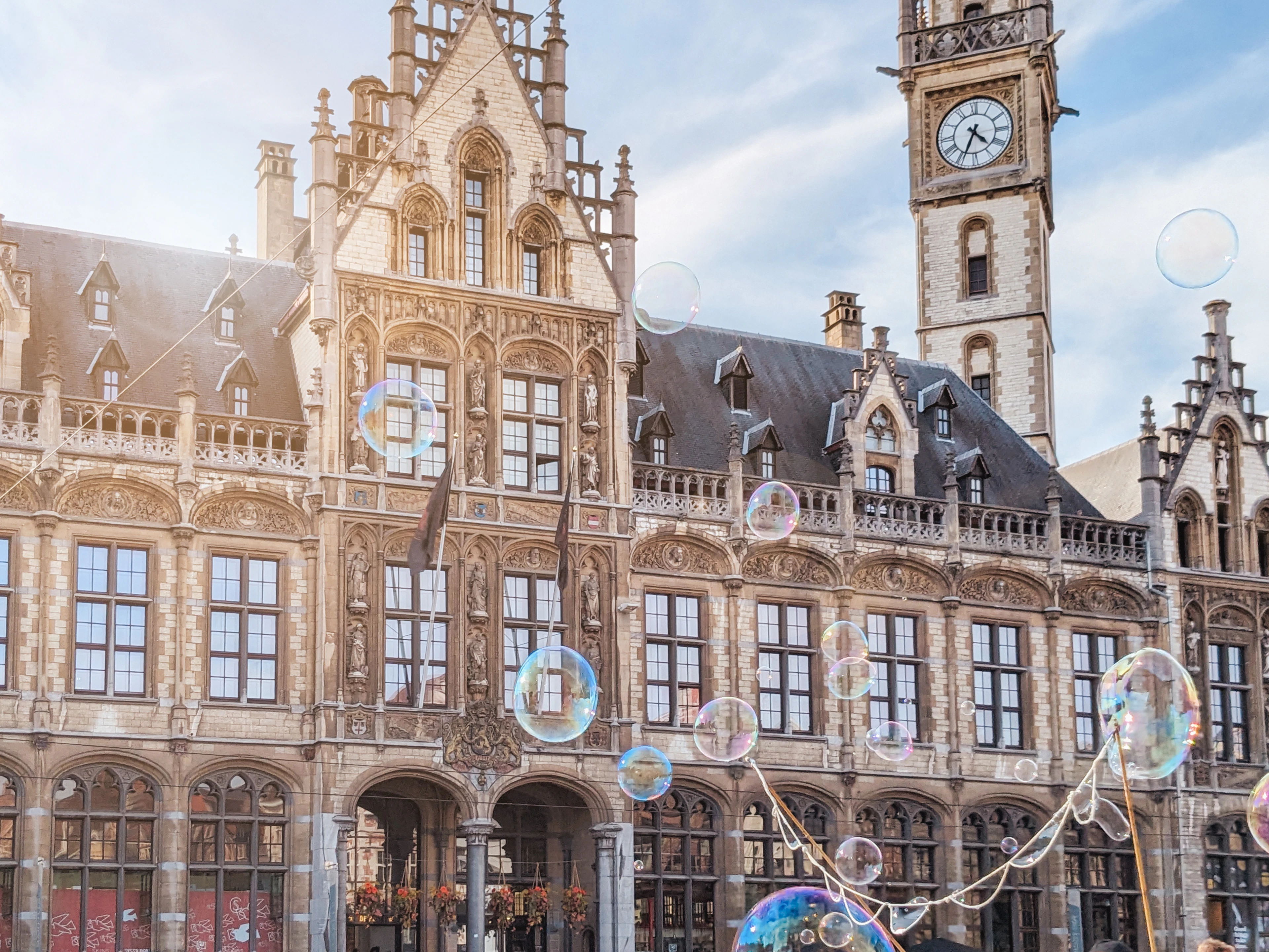 Ghent's neo-Gothic former Post Office building with its clock tower, soap bubbles drifting past the facade.