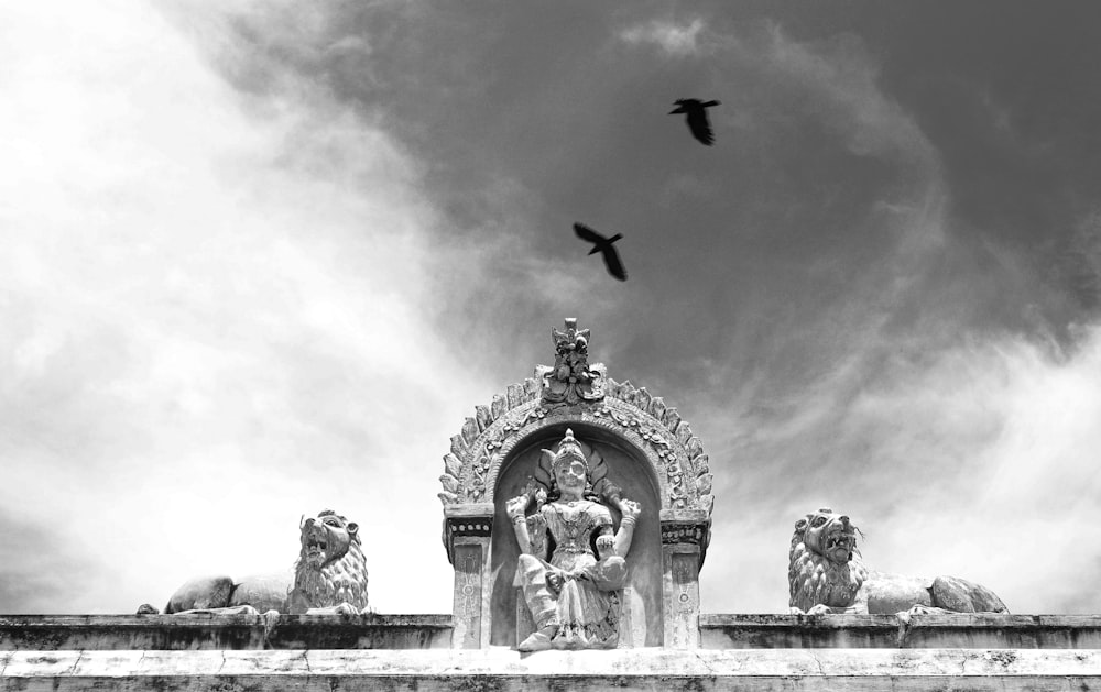 a black and white photo of a statue and birds