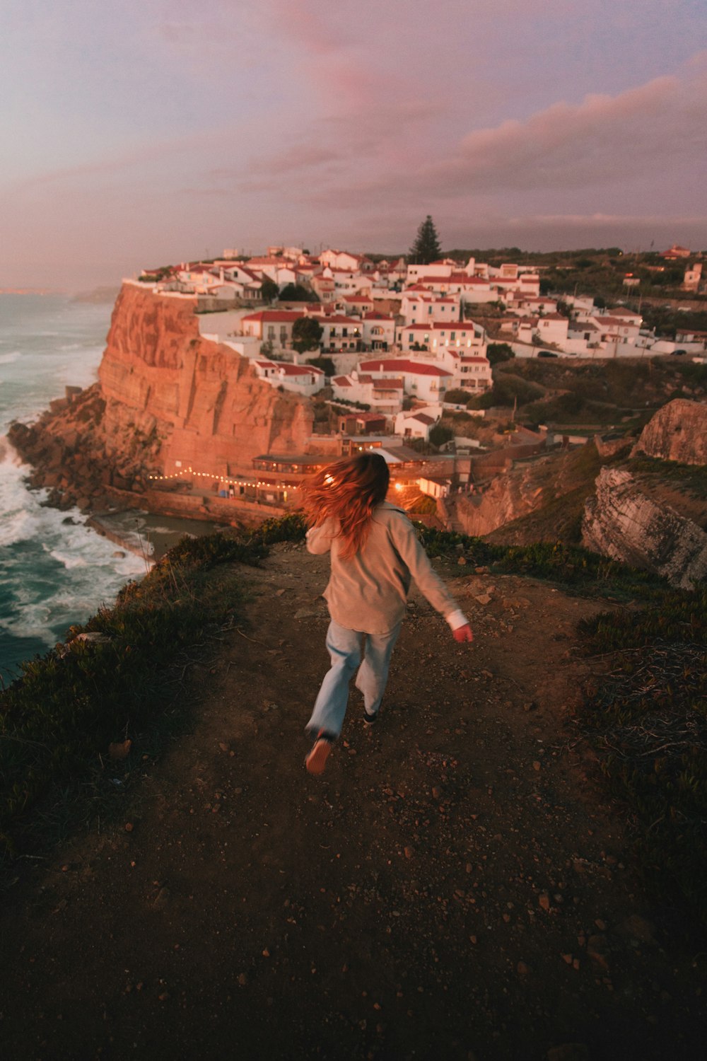 a woman running down a dirt road next to the ocean