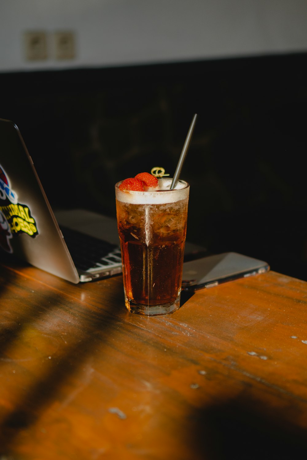 a drink sitting on top of a wooden table next to a laptop