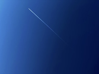 A clear blue sky is intersected by a thin, white contrail from a high-flying aircraft, creating a diagonal streak across the image.