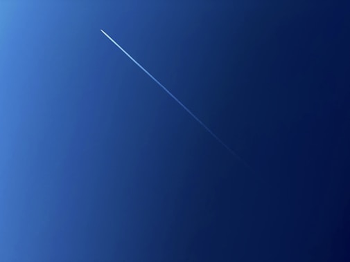 A clear blue sky is intersected by a thin, white contrail from a high-flying aircraft, creating a diagonal streak across the image.