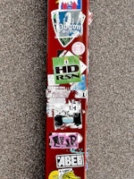 A red surface is covered with multiple colorful stickers, including logos, text, and designs. The background is a textured gray surface.