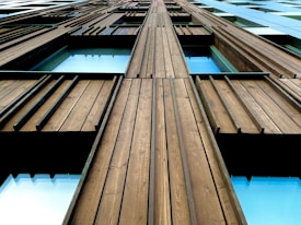 A close-up shot of a modern building's facade emphasizing vertical wooden panels and windows. The image captures the architectural details and materials used, showing the texture of the wood and the reflections in the glass windows.