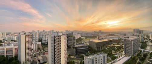 A panoramic cityscape featuring high-rise buildings and green spaces at sunset.