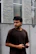 Image of a thoughtful man looking at a smartphone, standing against a minimalistic background.