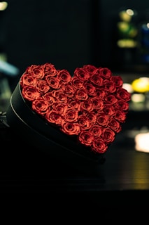 Artistic shot of a box of deep red roses tied with a subtle gold ribbon, resting on a sage green background.
