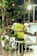 A traffic marshal is standing on the street wearing a bright yellow safety vest with reflective stripes, directing vehicles. The background shows an urban setting with blurred lights and a few cars, and the foreground includes some green foliage.
