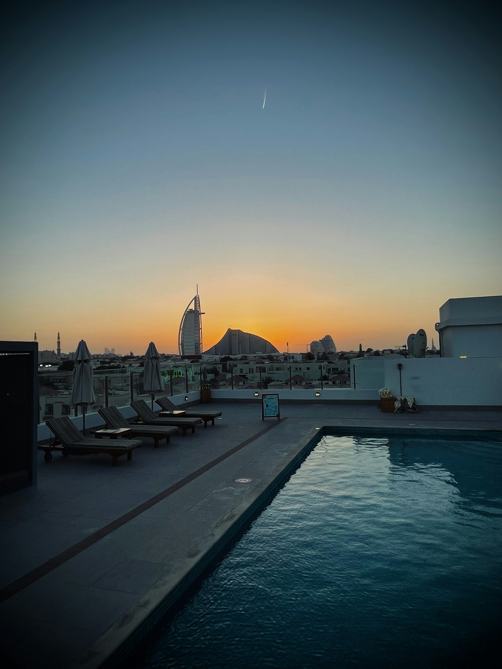 A serene rooftop pool area overlooking the Dubai Marina, bathed in warm evening light.
