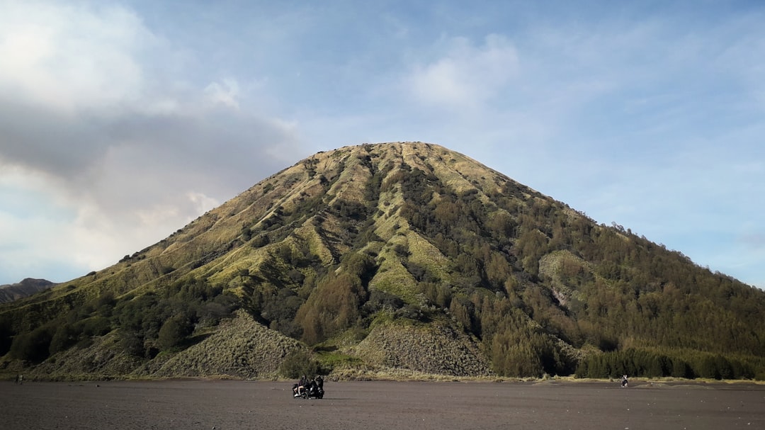 a motorcycle is parked in front of a mountain, Mount Batok (Gunung Batok) towering over the Bromo Caldera