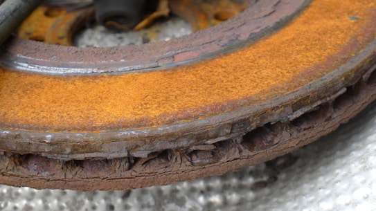 A rusty, deteriorated metal brake rotor with visible layers of corrosion and decay, the surface is heavily oxidized with a brownish-orange hue.