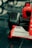 A close-up view of the front section of a red Formula 1 race car featuring a large black tire, branding and sponsorship logos such as FedEx, Bridgestone, and Shell on the white front wing. The car is displayed on a glossy, reflective surface.