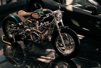 A custom-built motorcycle with polished metal components and intricate detailing, highlighted under soft lighting. The motorcycle features a shiny chrome engine, intricately designed exhaust pipes, and a light tan leather seat.