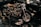 A custom-built motorcycle with polished metal components and intricate detailing, highlighted under soft lighting. The motorcycle features a shiny chrome engine, intricately designed exhaust pipes, and a light tan leather seat.