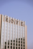 A tall building with a modern architectural style, featuring vertical glass panels and concrete sections. The top of the building displays large, stylized letters spelling 'ROME'. The sky above is clear and blue, creating a serene backdrop.