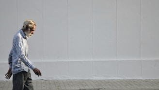 a man walking down a sidewalk with a white wall behind him