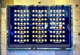 A framed poster with a grid of yellow stars against a dark blue background, accompanied by names of various newspapers and publications. Each row features publications such as The Times, Evening Standard, and others, each followed by a corresponding row of yellow stars.