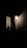 A wall-mounted lampshade illuminates a dark area, casting a soft glow on a textured wall. Nearby, electrical wiring and a device are attached to the wall, partially visible in the subdued light.