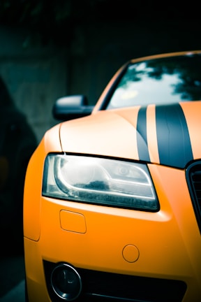 Close-up of a matte black Challenger hood with bold orange racing stripes under bright sunlight.