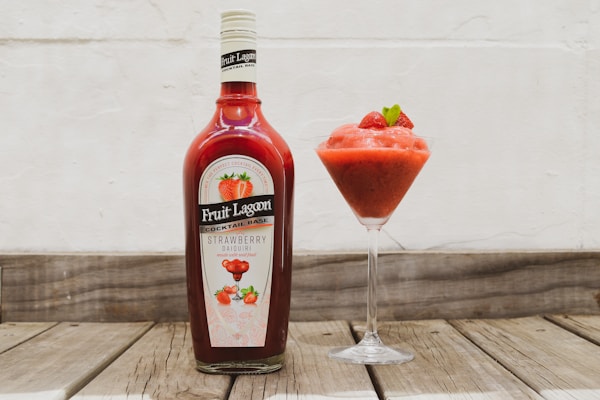 A bottle of fruit jam next to a glass of strawberry juice