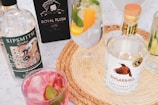An assortment of gin bottles and cocktails is arranged on a woven placemat. Sipsmith and Sugarbird gin bottles are prominently displayed alongside glasses filled with colorful cocktails garnished with fruit and mint leaves.