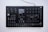 A black electronic music synthesizer with numerous knobs, buttons, and a small display screen in the center. It features labeled controls for various functions like volume, tempo, and different sound effects. The device appears to be designed for complex audio manipulation and production.