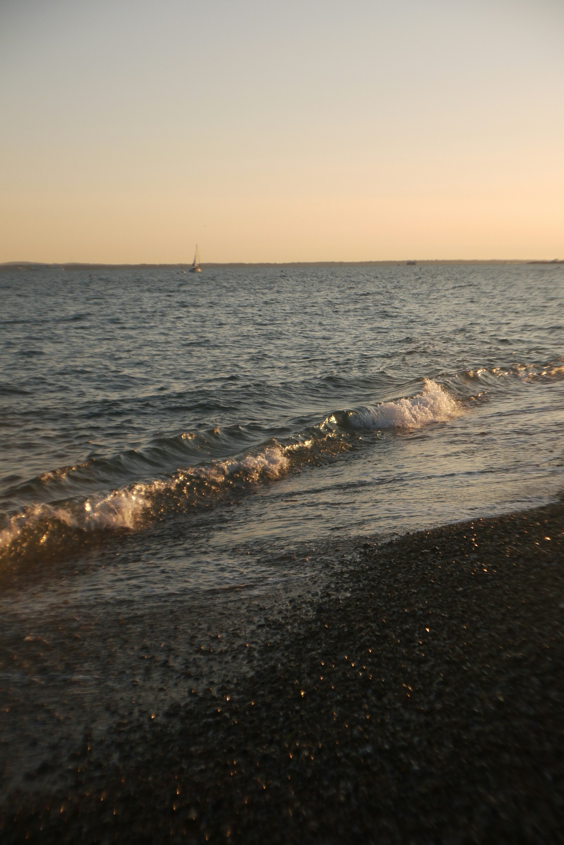 a beach with waves coming in to shore and a sailboat in the distance