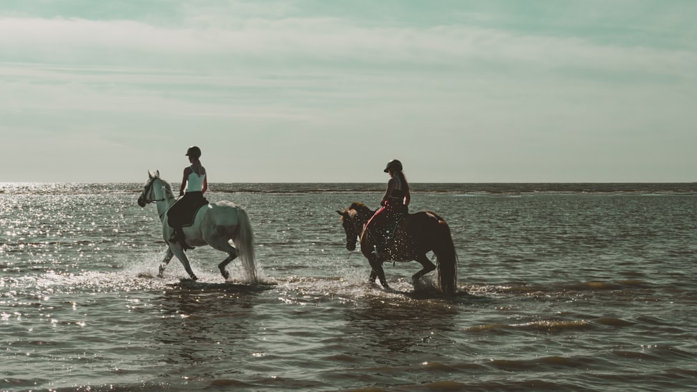 two people are riding horses through the water
