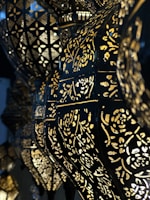 Ornate lamps with intricate cut-out patterns allow light to shine through, creating an elegant, geometric and floral design. The dark metal contrasts with the golden glow of the lights, enhancing the decorative patterns.