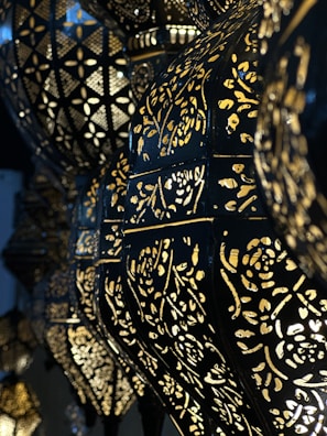 Ornate lamps with intricate cut-out patterns allow light to shine through, creating an elegant, geometric and floral design. The dark metal contrasts with the golden glow of the lights, enhancing the decorative patterns.