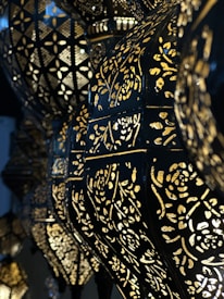 Ornate lamps with intricate cut-out patterns allow light to shine through, creating an elegant, geometric and floral design. The dark metal contrasts with the golden glow of the lights, enhancing the decorative patterns.