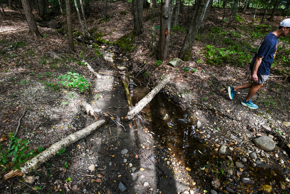 a man walking through a forest next to a creek