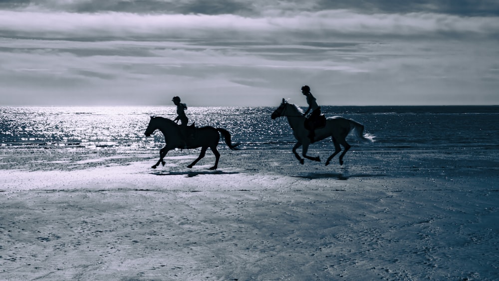 two people riding horses on a beach near the ocean