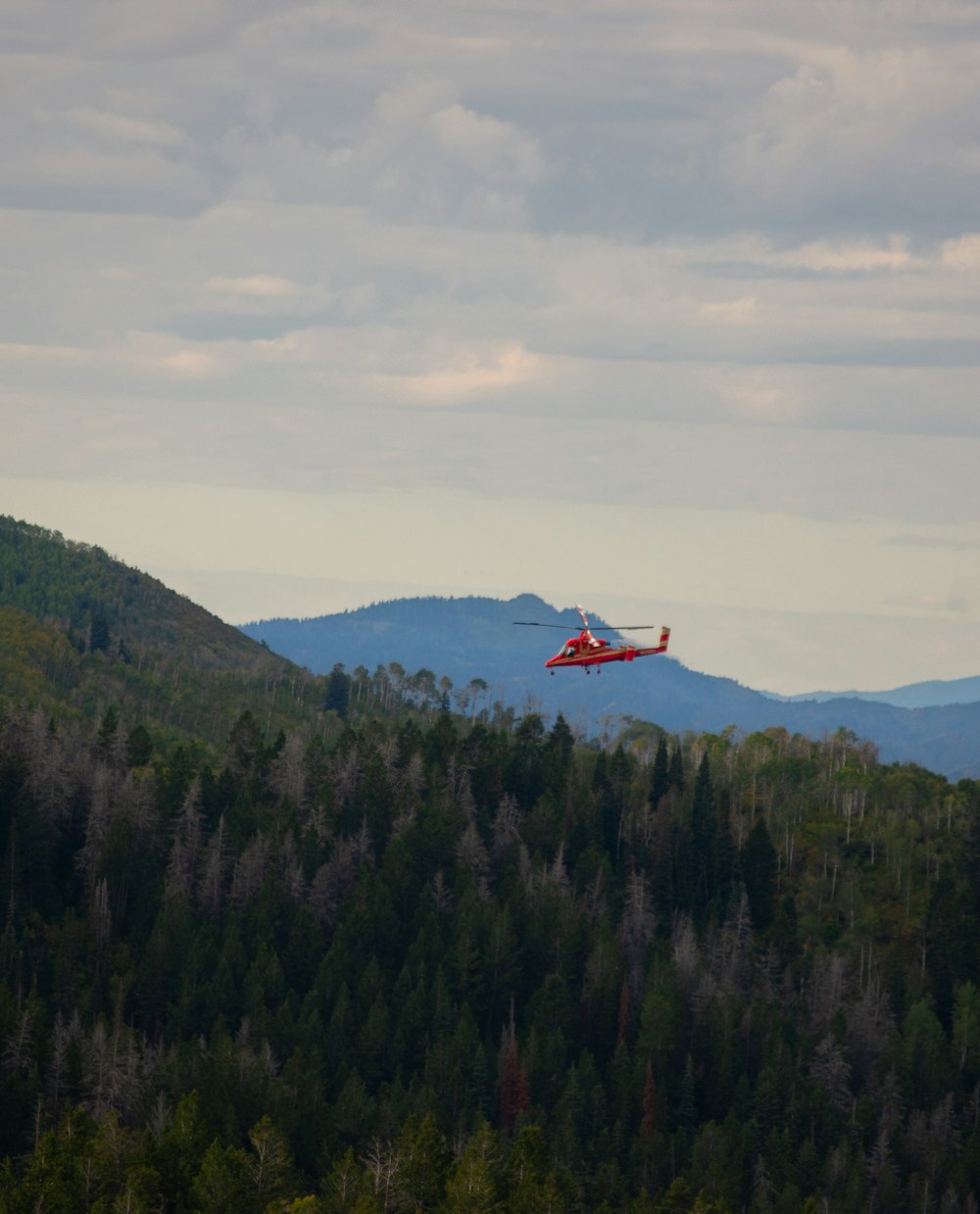 a red helicopter flying over a lush green forest