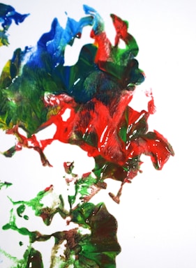 A vibrant and abstract mix of swirling colors, including red, green, blue, and hints of yellow, creates a dynamic pattern against a white background. The paint appears thick and textured, giving a sense of movement and energy.