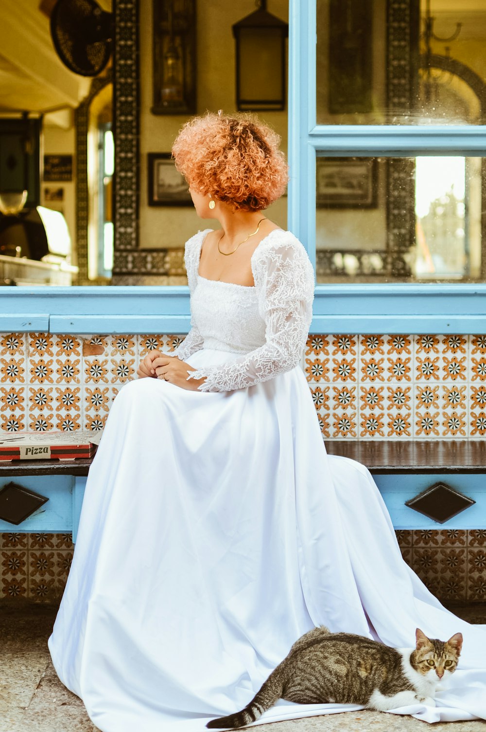 a woman in a white dress sitting on a bench next to a cat