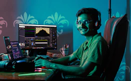 Friendly author smiling while writing at a desk surrounded by tech gadgets.