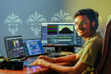 Smiling Indian video editor with headphones working on a laptop and monitor