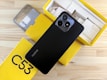 A smartphone with a black back featuring dual camera lenses is placed atop a partially open yellow box. The box is labeled 'C53' and contains various accessories, such as a charger and cables. A protective phone case is also visible beside the box.
