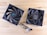 Two black computer cooling fans are placed on a light wooden surface. The fans have multiple blades and visible wires. One fan displays branding and specifications on the central hub.