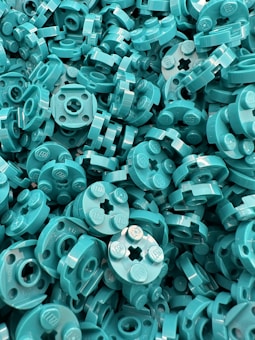 A dense collection of turquoise LEGO pieces piled together, showcasing their uniform round and cylindrical shapes with an embossed logo.