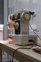 A compact portable sewing machine placed on a wooden table with sewing accessories.