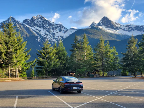 A sleek private taxi vehicle parked in front of snowy alpine mountains at sunrise.