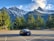 A sleek private taxi vehicle parked with snowy alpine mountains in the background under a clear blue sky.