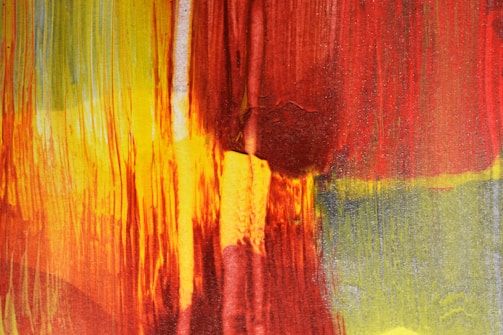 Vividly colored abstract painting with vibrant streaks of red, yellow, and hints of green. The colors are blended in an expressive manner, creating a textured and dynamic appearance.